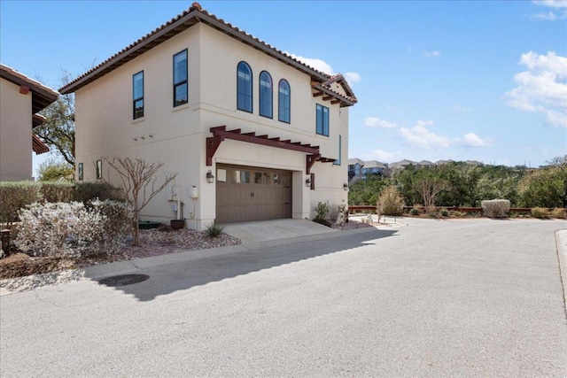 view of front facade featuring driveway, an attached garage, a tiled roof, and stucco siding