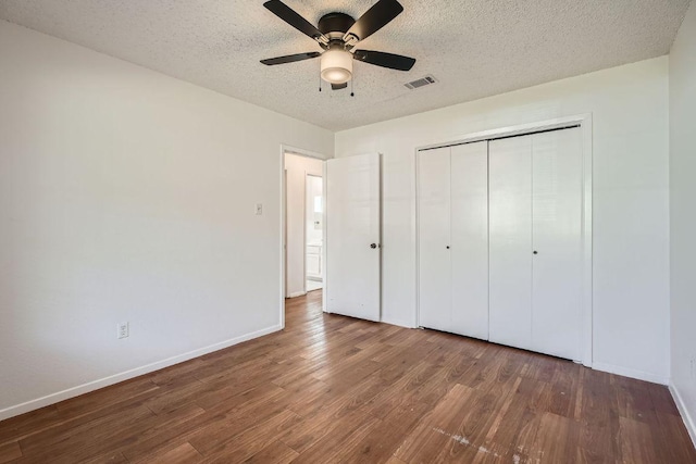 unfurnished bedroom featuring a textured ceiling, wood finished floors, visible vents, baseboards, and a closet