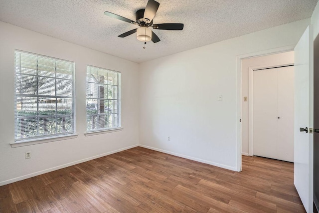 empty room with a ceiling fan, a textured ceiling, baseboards, and wood finished floors