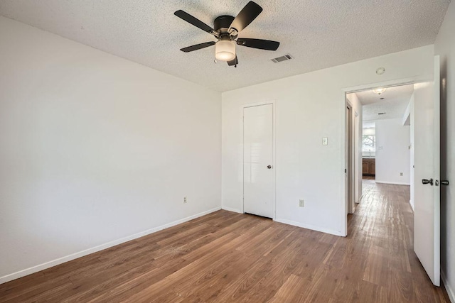 unfurnished bedroom with baseboards, a textured ceiling, visible vents, and wood finished floors