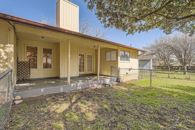 rear view of house with french doors, a patio, a chimney, fence, and a yard