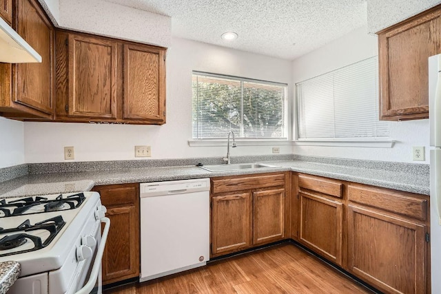 kitchen with a textured ceiling, white appliances, a sink, light wood-style floors, and brown cabinets