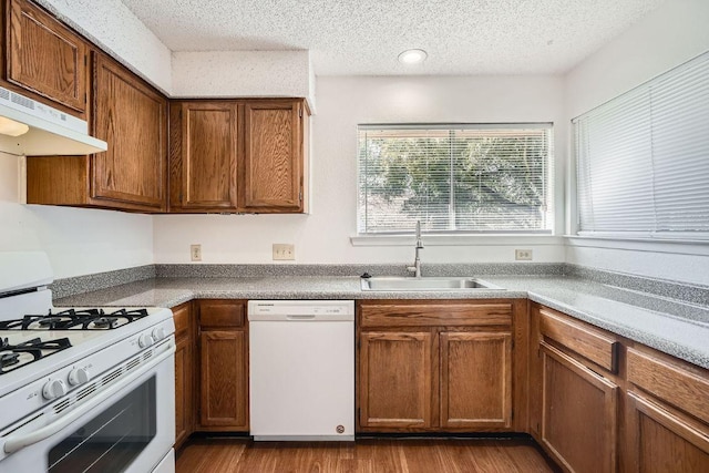 kitchen featuring brown cabinetry, a sink, a textured ceiling, white appliances, and under cabinet range hood