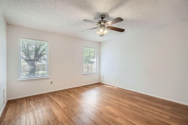 empty room with light wood-style floors, a textured ceiling, and baseboards