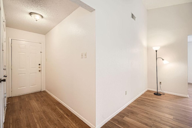 corridor with baseboards, a textured ceiling, visible vents, and wood finished floors