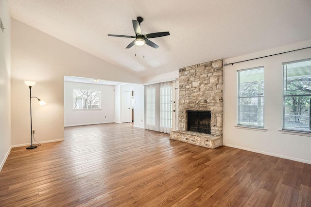 unfurnished living room with a ceiling fan, lofted ceiling, a stone fireplace, and wood finished floors