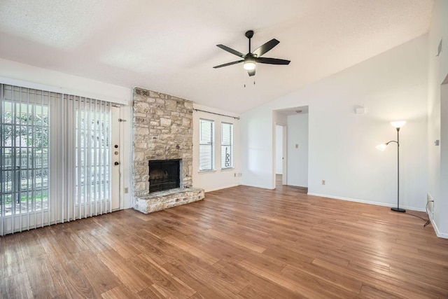 unfurnished living room featuring lofted ceiling, plenty of natural light, a stone fireplace, and wood finished floors