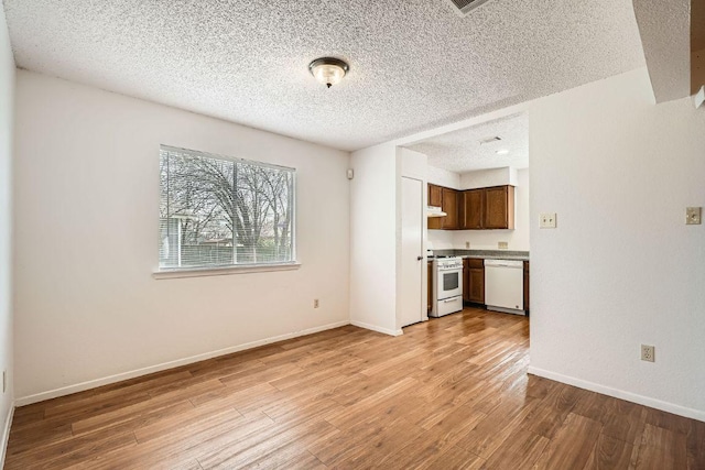 unfurnished living room with a textured ceiling, light wood-type flooring, and baseboards