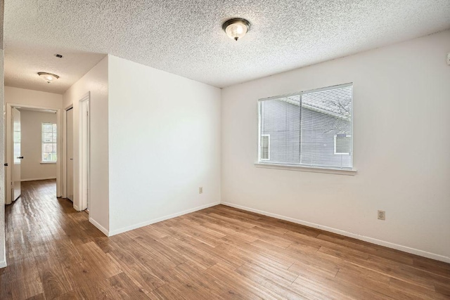 unfurnished room with a textured ceiling, baseboards, and wood finished floors