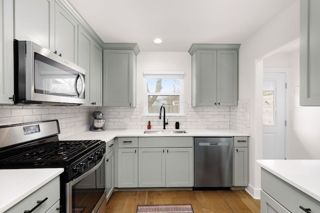 kitchen featuring stainless steel appliances, gray cabinets, light countertops, and a sink