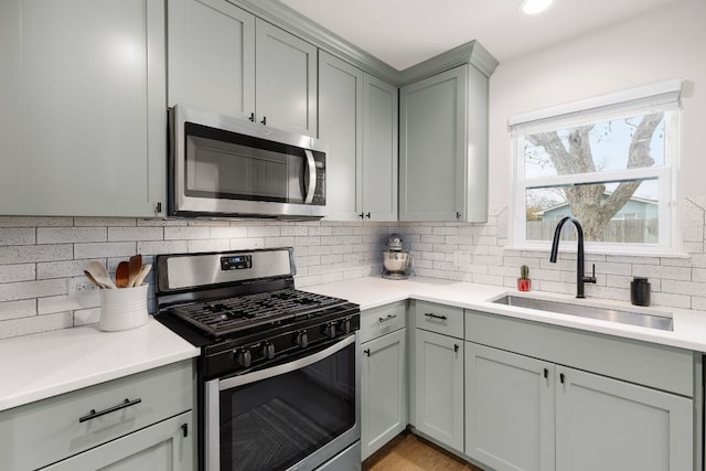 kitchen with tasteful backsplash, gray cabinets, stainless steel appliances, and a sink