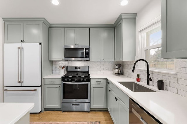 kitchen with a sink, appliances with stainless steel finishes, gray cabinets, decorative backsplash, and light wood finished floors