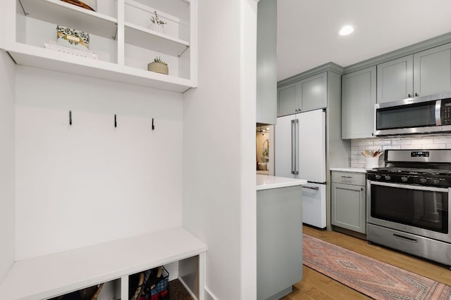 kitchen featuring light wood finished floors, appliances with stainless steel finishes, gray cabinets, light countertops, and backsplash