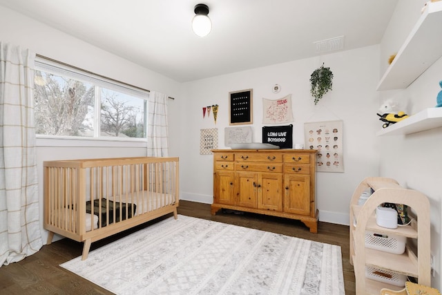 bedroom featuring a crib, dark wood-style floors, baseboards, and visible vents