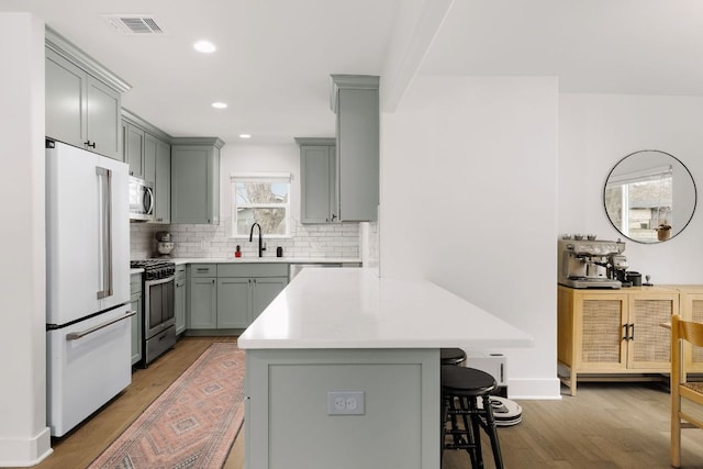 kitchen with a breakfast bar area, appliances with stainless steel finishes, gray cabinets, and a sink