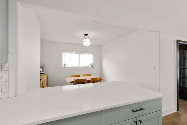 kitchen with light stone counters, wood finished floors, visible vents, and decorative light fixtures