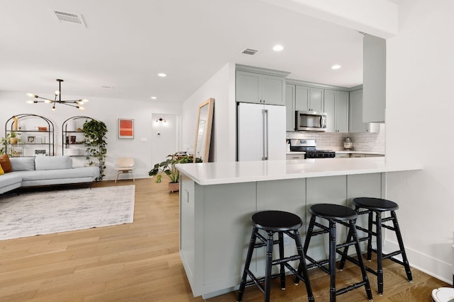 kitchen with visible vents, decorative backsplash, gray cabinetry, appliances with stainless steel finishes, and a kitchen breakfast bar