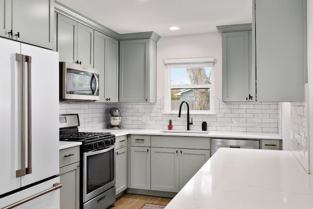 kitchen with stainless steel appliances, decorative backsplash, a sink, and gray cabinetry