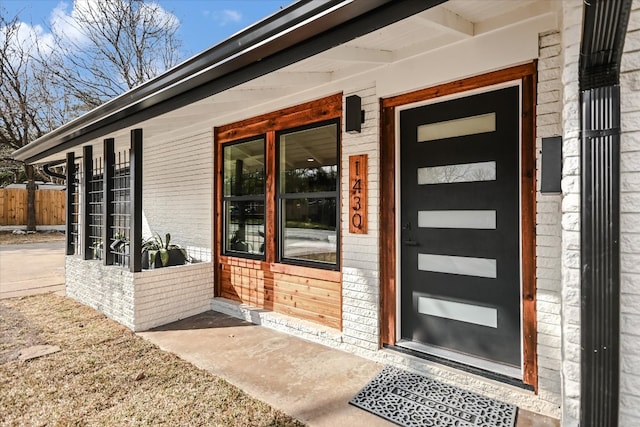 property entrance with a porch, brick siding, and fence