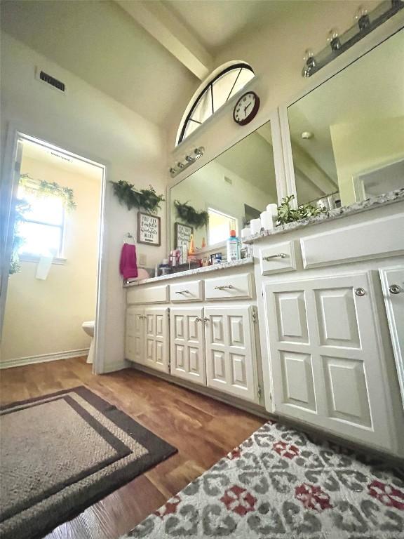 bathroom with vaulted ceiling with beams, double vanity, visible vents, toilet, and wood finished floors