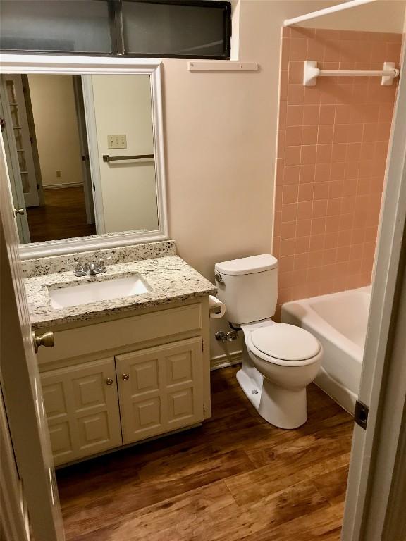 bathroom with washtub / shower combination, vanity, wood finished floors, and toilet