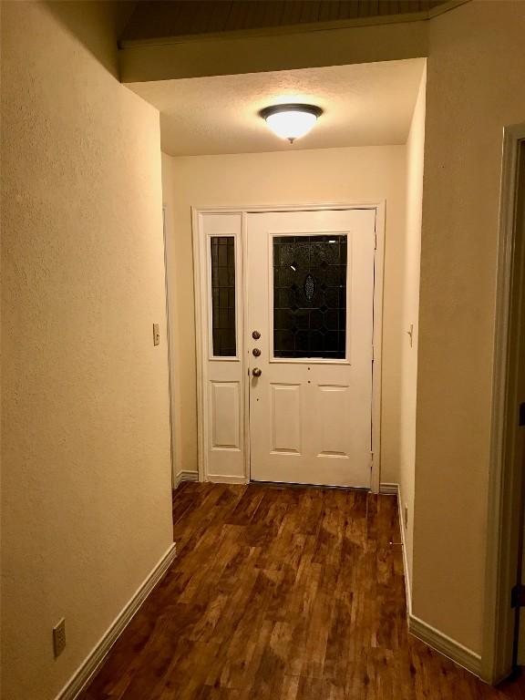 doorway with a textured wall, dark wood-type flooring, and baseboards