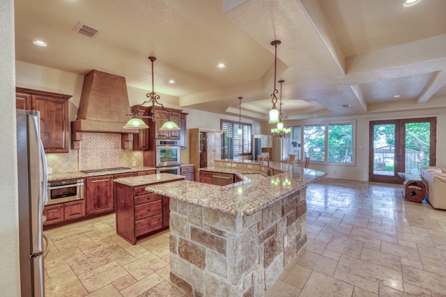 kitchen with stone tile floors, custom exhaust hood, stainless steel appliances, visible vents, and a large island with sink