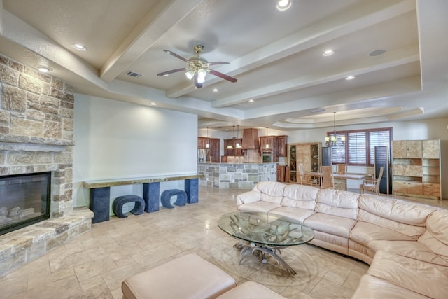 living area featuring beam ceiling, a fireplace, stone tile flooring, visible vents, and a raised ceiling