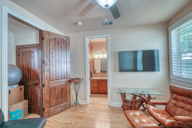 sitting room featuring visible vents, a textured wall, ceiling fan, a textured ceiling, and light wood-type flooring