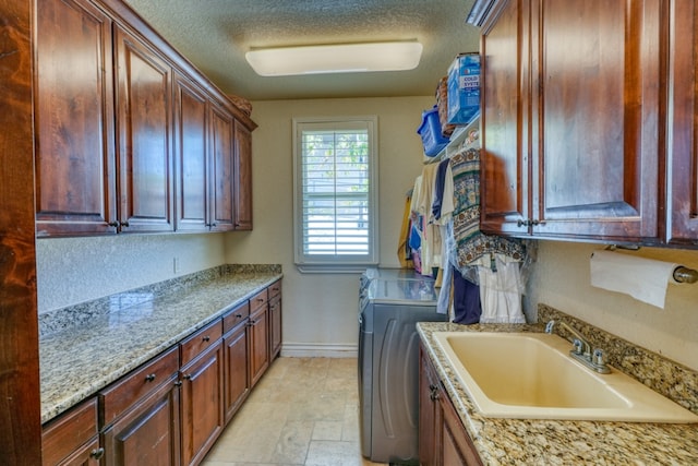 washroom featuring cabinet space, baseboards, a textured ceiling, washer and dryer, and a sink