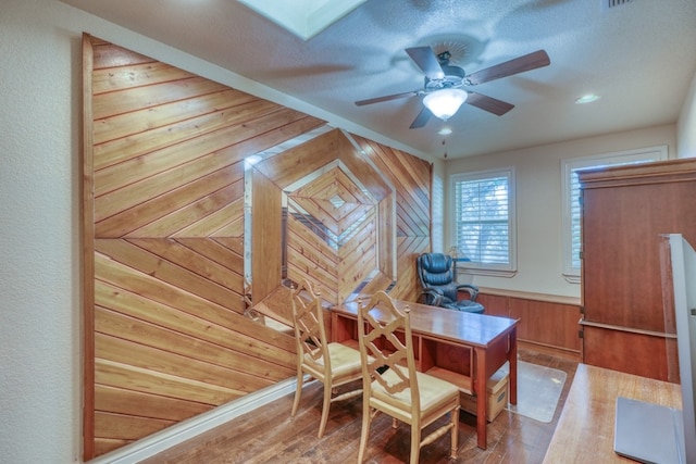 office with a skylight, wooden walls, a ceiling fan, a wainscoted wall, and wood finished floors