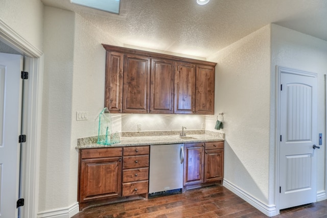 kitchen with dishwasher, a textured wall, light stone counters, and dark wood finished floors