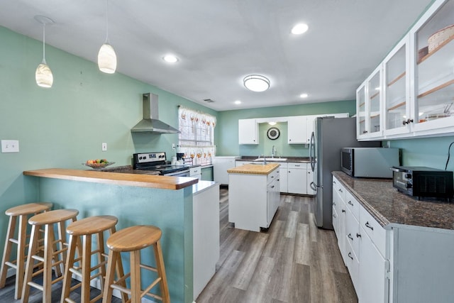 kitchen featuring a peninsula, a sink, wood finished floors, wall chimney range hood, and appliances with stainless steel finishes