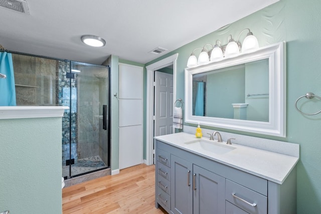 full bathroom with wood finished floors, a shower stall, and visible vents