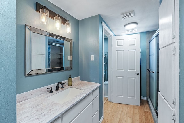 bathroom with vanity, an enclosed shower, wood finished floors, and visible vents