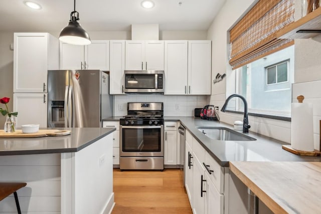 kitchen with light wood-style flooring, stainless steel appliances, a sink, tasteful backsplash, and pendant lighting