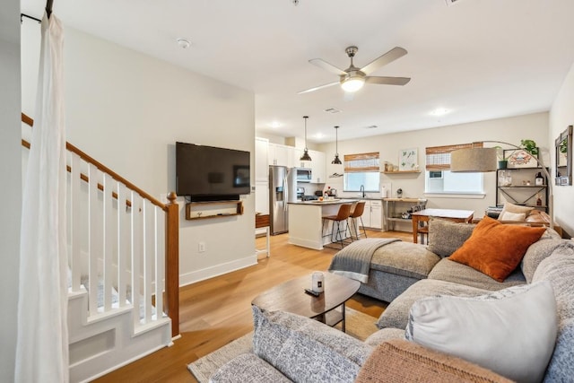 living room featuring baseboards, light wood-style flooring, and a ceiling fan