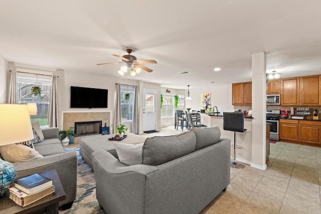 living area with recessed lighting, a tiled fireplace, a ceiling fan, light tile patterned flooring, and baseboards