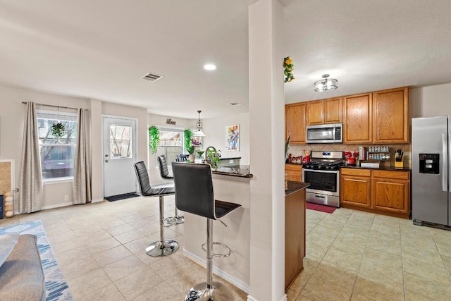 kitchen with visible vents, dark countertops, appliances with stainless steel finishes, a breakfast bar area, and backsplash