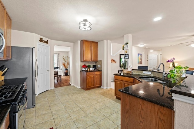 kitchen with light tile patterned floors, a sink, brown cabinets, stainless steel gas stove, and dark stone countertops