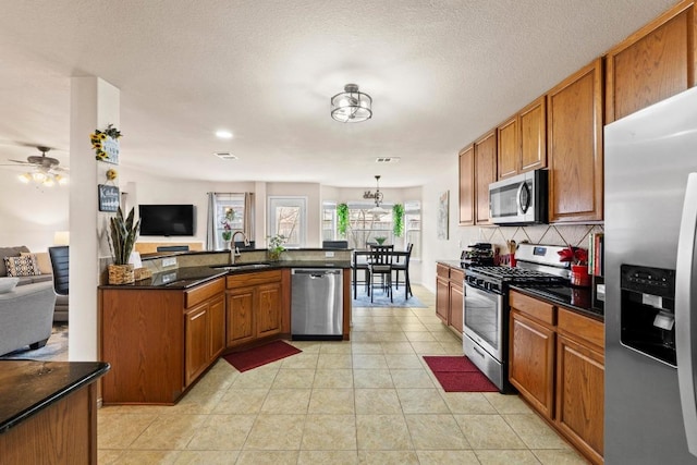 kitchen featuring stainless steel appliances, a sink, open floor plan, tasteful backsplash, and brown cabinetry