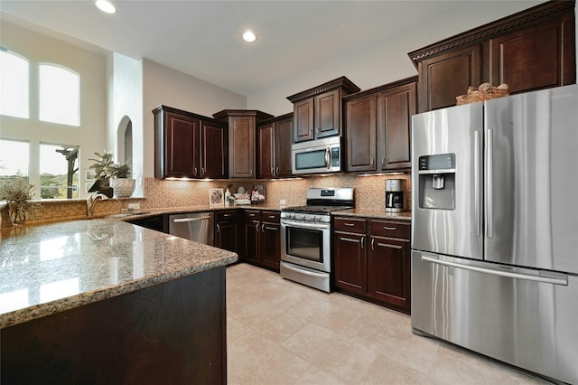 kitchen featuring dark brown cabinetry, light stone countertops, appliances with stainless steel finishes, and backsplash