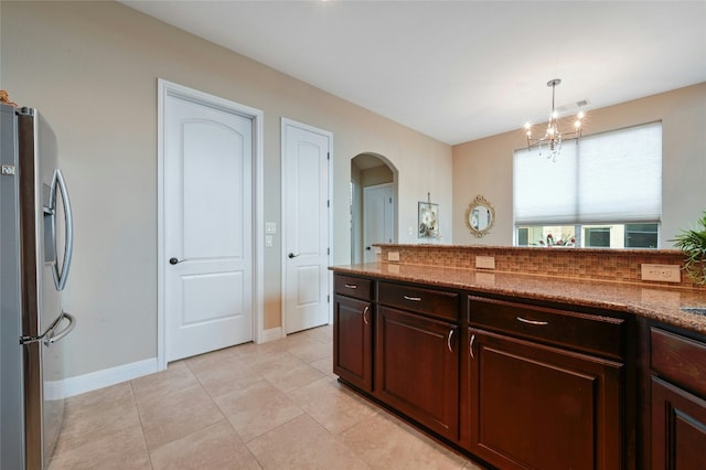 kitchen with arched walkways, decorative light fixtures, stainless steel refrigerator with ice dispenser, light tile patterned floors, and dark brown cabinets