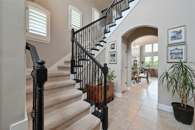 entrance foyer with arched walkways, light tile patterned floors, a towering ceiling, baseboards, and stairway