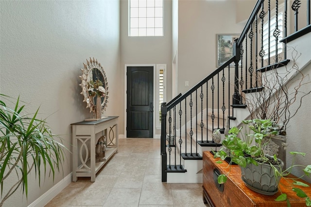 tiled entrance foyer featuring a towering ceiling, baseboards, and stairway