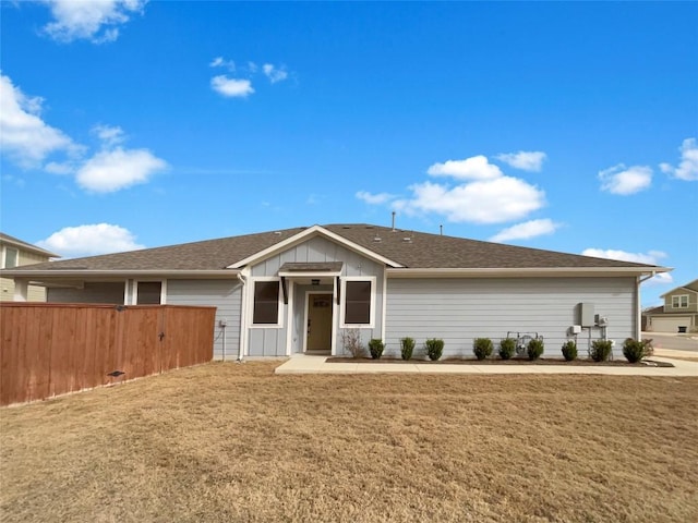 ranch-style home featuring roof with shingles, fence, board and batten siding, and a front yard