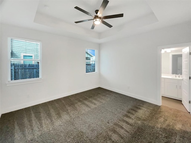 unfurnished bedroom featuring carpet floors, a tray ceiling, a sink, and baseboards