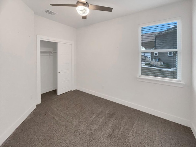 unfurnished bedroom with a closet, visible vents, dark carpet, a ceiling fan, and baseboards