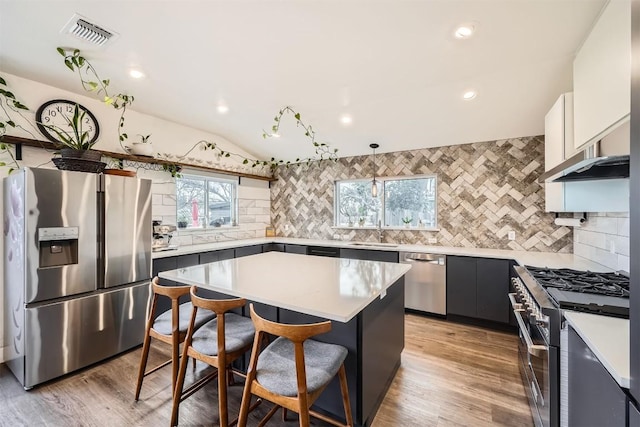 kitchen featuring stainless steel appliances, visible vents, a kitchen breakfast bar, light countertops, and a center island