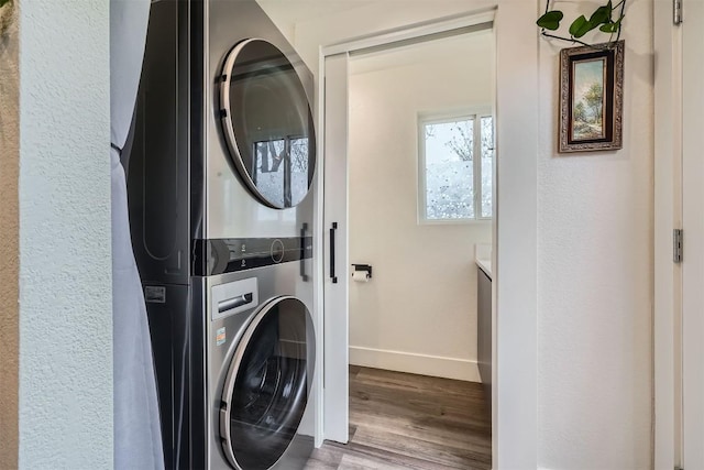 laundry room featuring laundry area, wood finished floors, stacked washer and clothes dryer, and baseboards